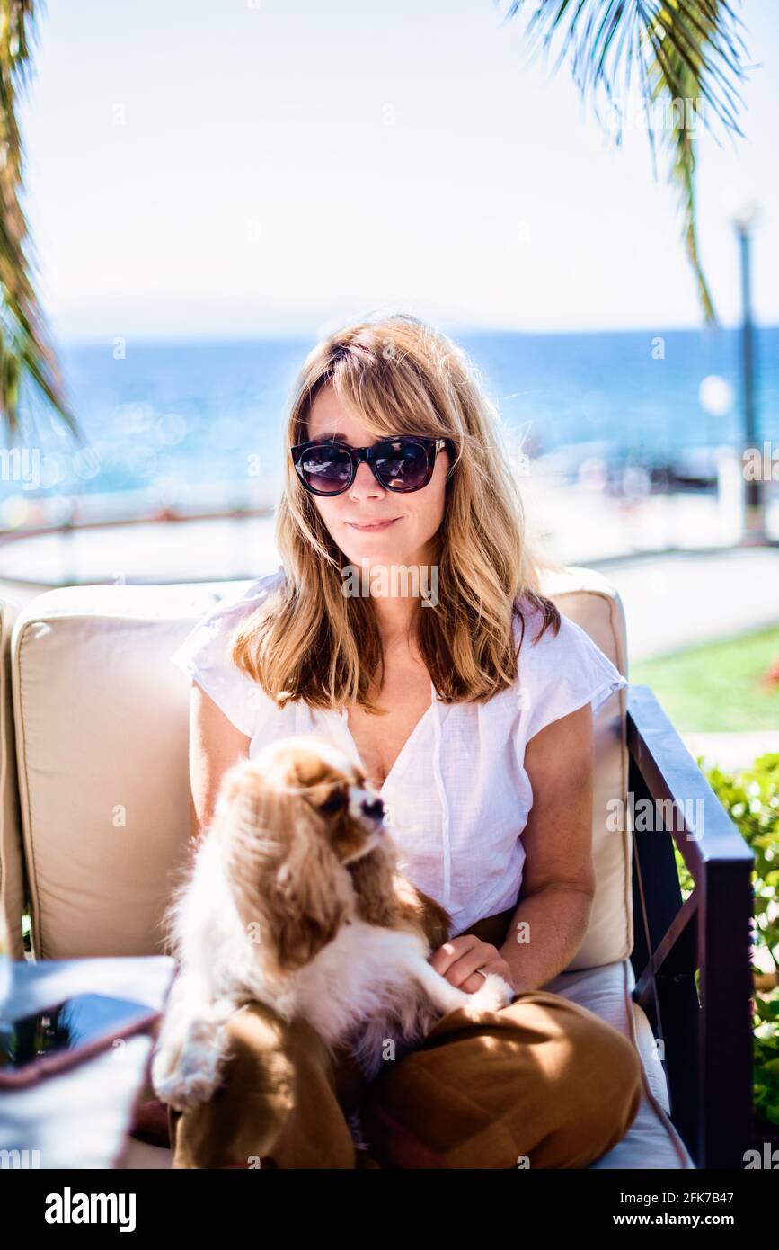 Foto di donna di mezza età godendo di una giornata di sole mentre si rilassa sul mare con simpatico cucciolo. Foto Stock