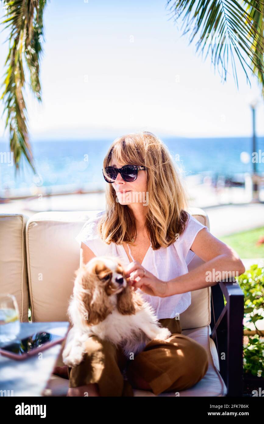 Foto di donna di mezza età godendo di una giornata di sole mentre si rilassa sul mare con simpatico cucciolo. Foto Stock