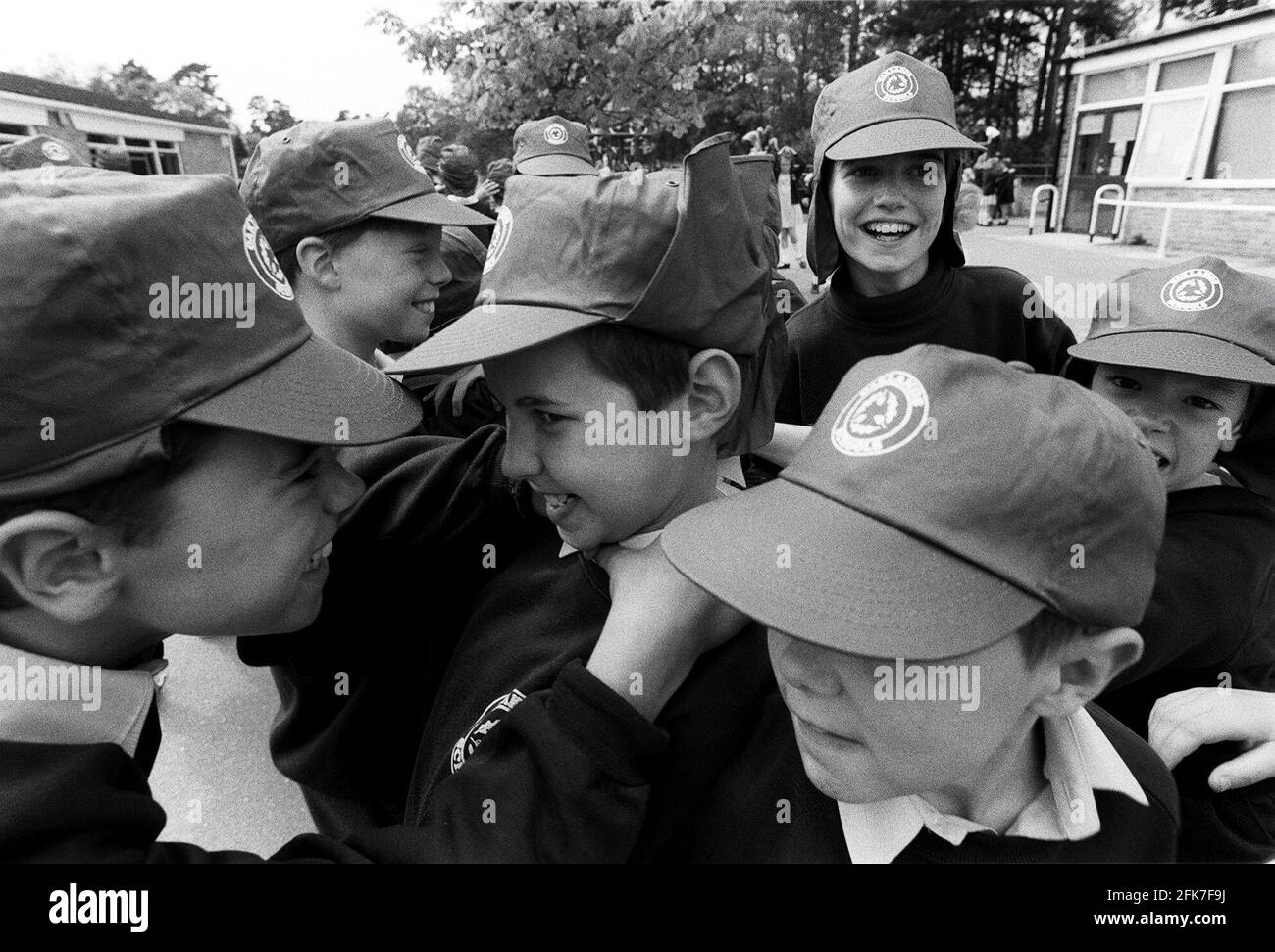 Alcuni giovani e vivaci scolaresche vanno selvaggiamente nel parco giochi a. rompere indossando i loro nuovi cappelli scuola Foto Stock