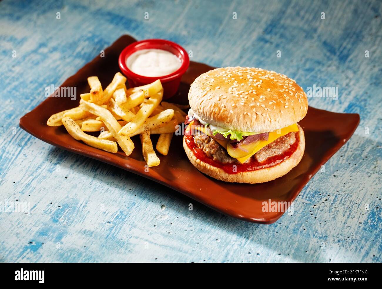 Hamburger. Succulenti cotolette di maiale, formaggio cheddar, cipolle croccanti sottaceto, lattuga avvolta in un panino sotto due salse. Servito con patatine fritte e salsa alla panna. Foto Stock