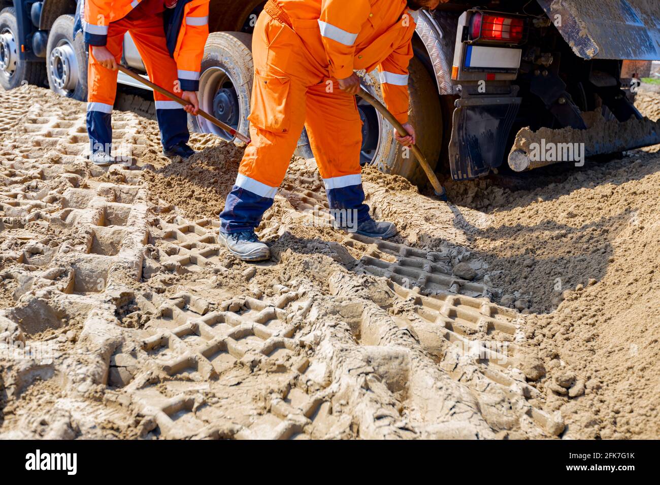 I lavoratori utilizzano pale, per scavare intorno alle ruote dei camion, per aiutarlo a uscire dalla sabbia nel cantiere. Foto Stock