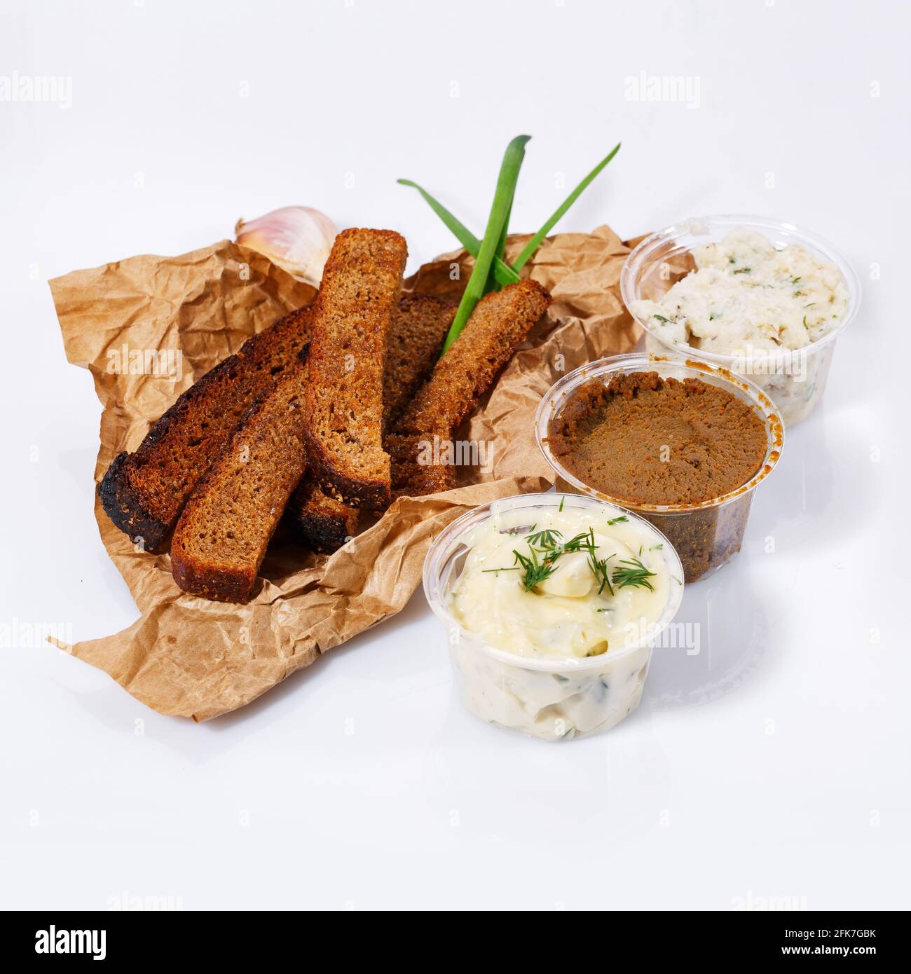 Cracker di pane nero giacciono su carta kraft, maionese e salsa all'aglio, pate di carne, strutto con aneto su sfondo bianco. Vista laterale. Foto Stock