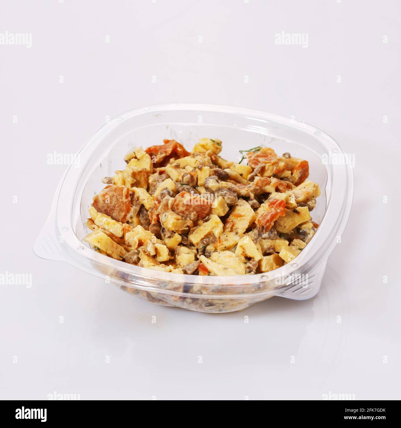 Insalata di carote, carne, formaggio e salsa in un recipiente di plastica trasparente su fondo bianco. Piatto gustoso. Foto Stock