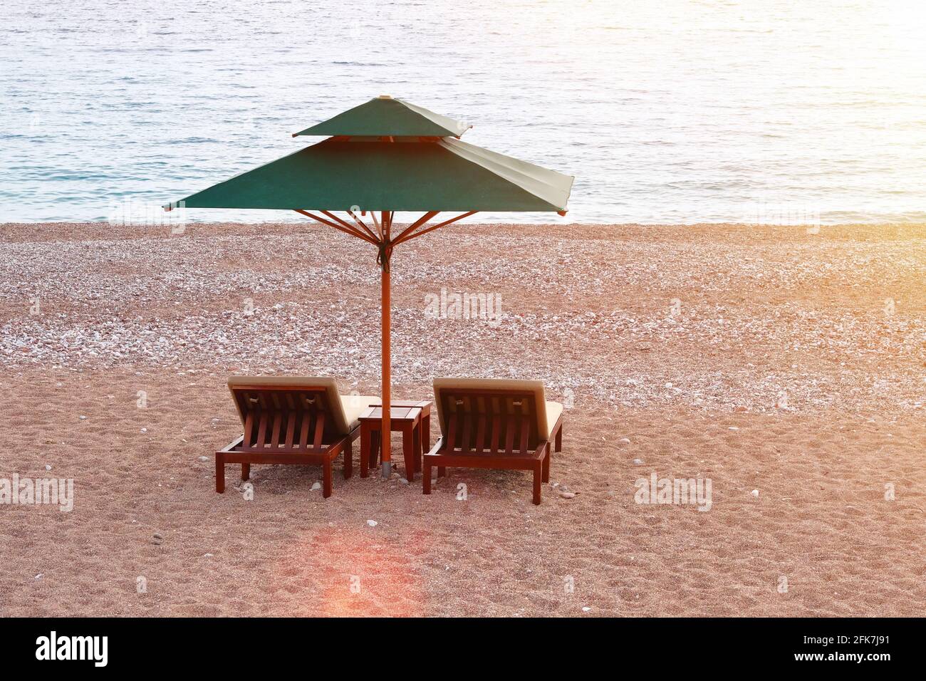 Sedie a sdraio con ombrellone sulla spiaggia. Concetto di vacanza perfetto. Mare blu e cielo con luce solare giallo tenue su sfondo. Riposa con comodità. Foto Stock
