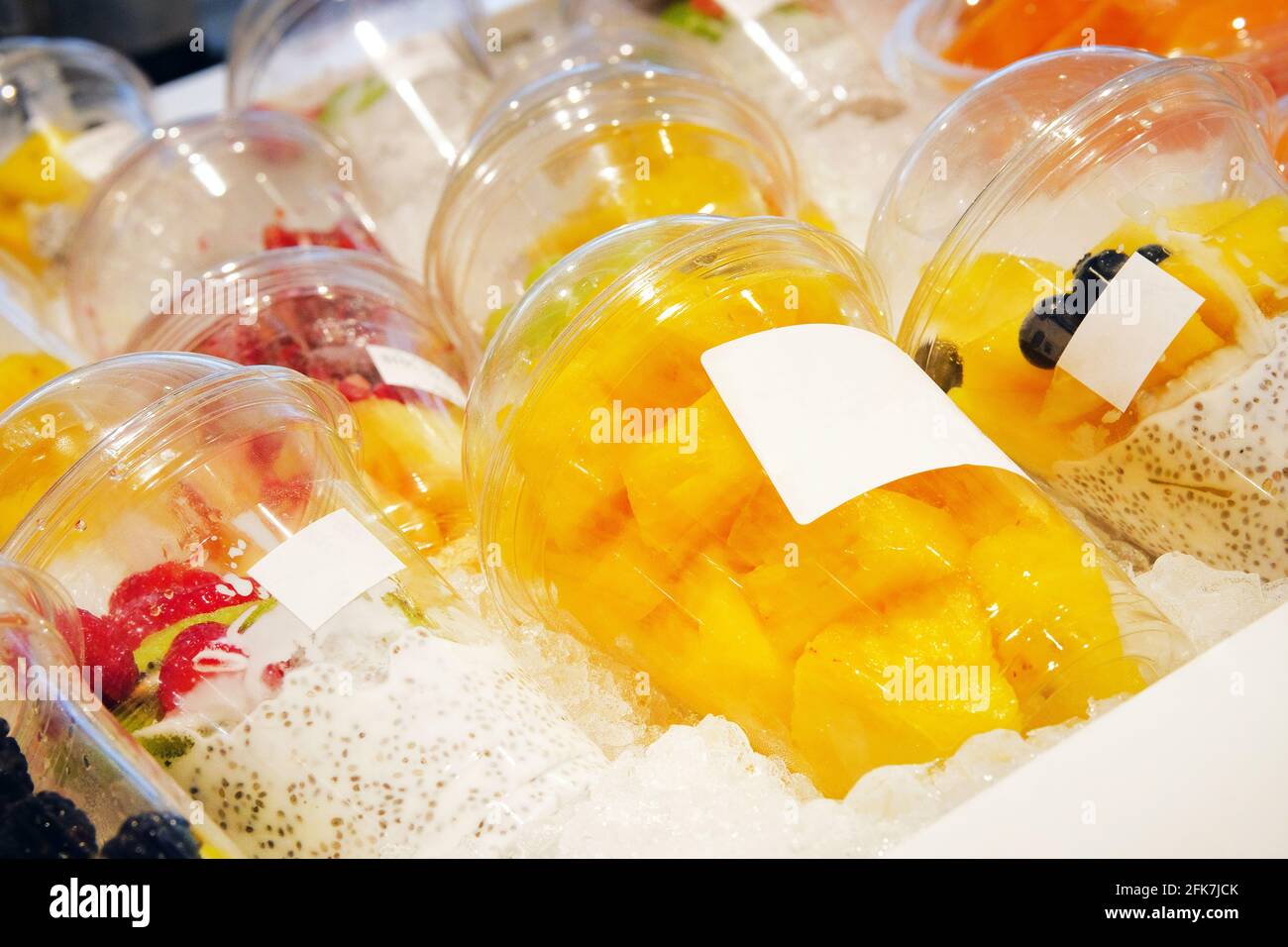 Pezzi di ananas e di altri frutti con lo yogurt di semi di chia sono disposti in tazze monouso di plastica e venduti in negozio. Cibi vegetariani sani concep Foto Stock