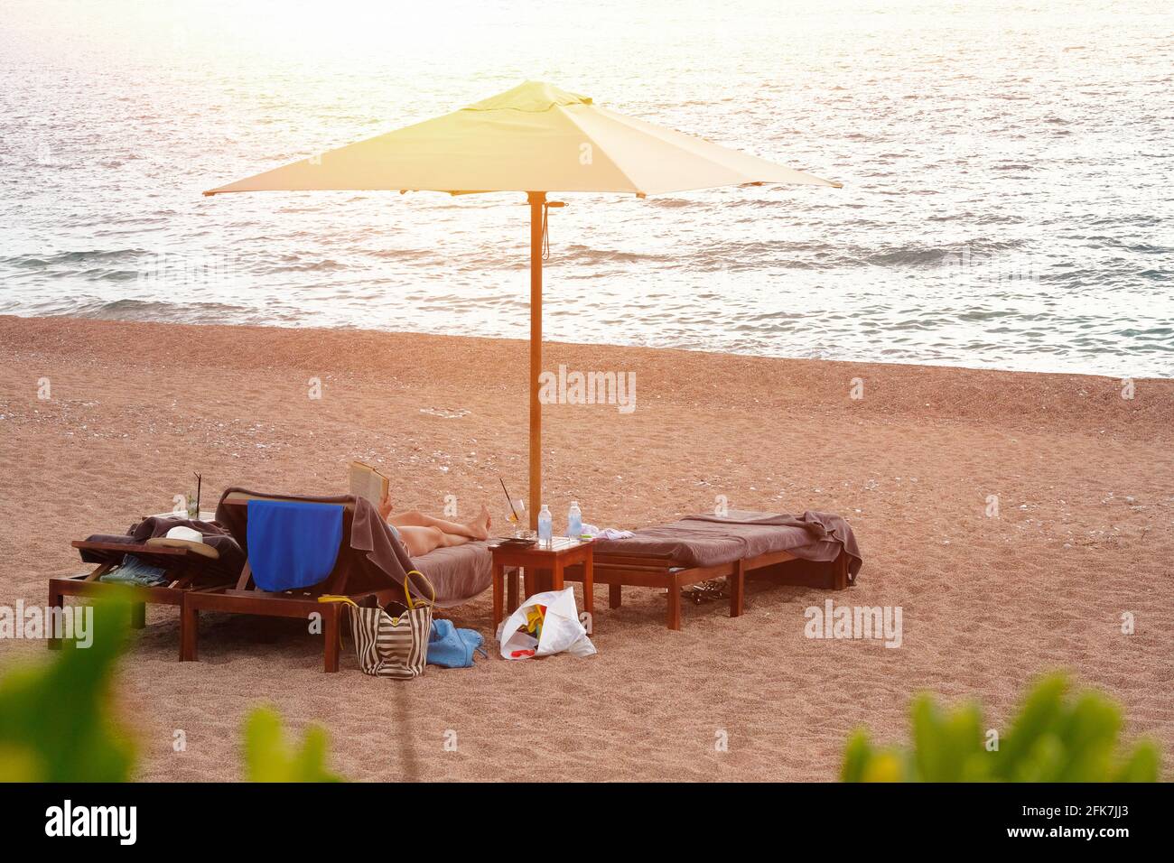 Donna che riposa comodamente sui lettini sotto l'ombrellone bianco. Concetto di vacanza perfetto. Luce solare giallo tenue. Foto candida. Foto Stock
