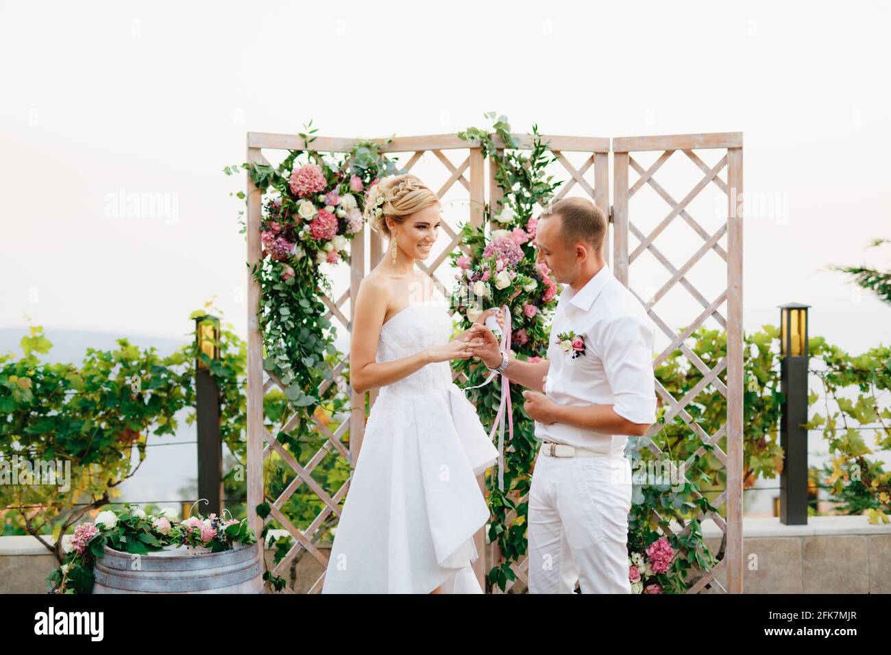 La sposa e lo sposo stanno vicino all'arco del matrimonio, lo sposo mette l'anello sul dito della sposa durante la cerimonia nuziale Foto Stock