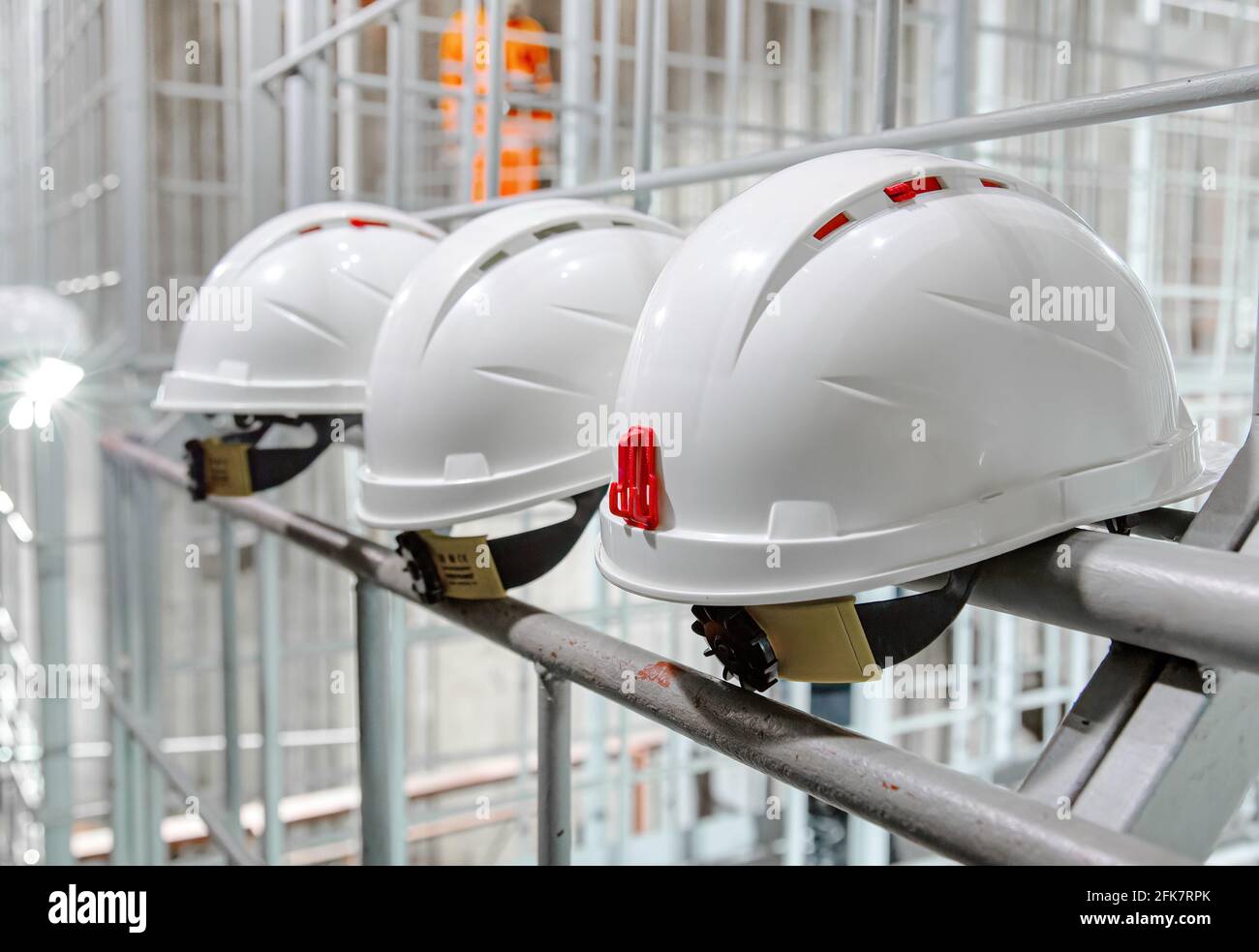 Caschi di sicurezza bianchi appesi a parete alla fabbrica. Bretella di fissaggio bianca di sicurezza per tecnici edili Foto Stock