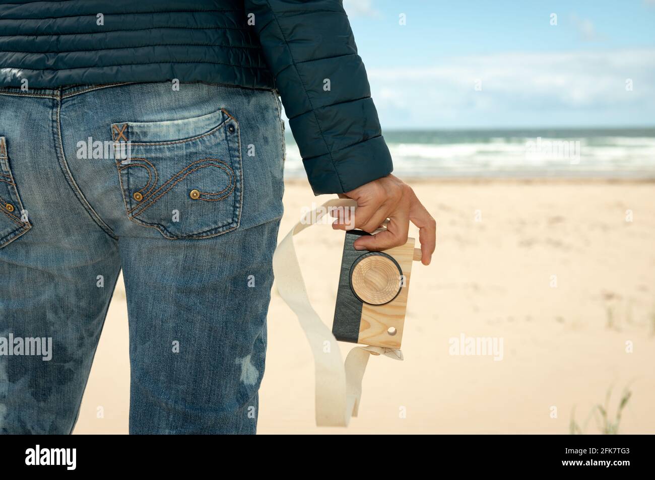 Primo piano della mano della donna che tiene una macchina fotografica giocattolo di legno sullo sfondo della spiaggia sabbiosa. Concetto di fotografia divertente. Foto Stock