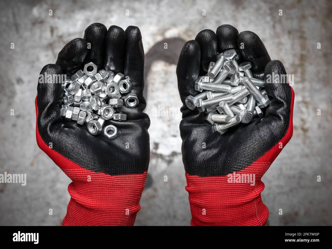 La persona che indossa guanti protettivi che tengono una manciata di bulloni e. dadi su fondo metallico Foto Stock