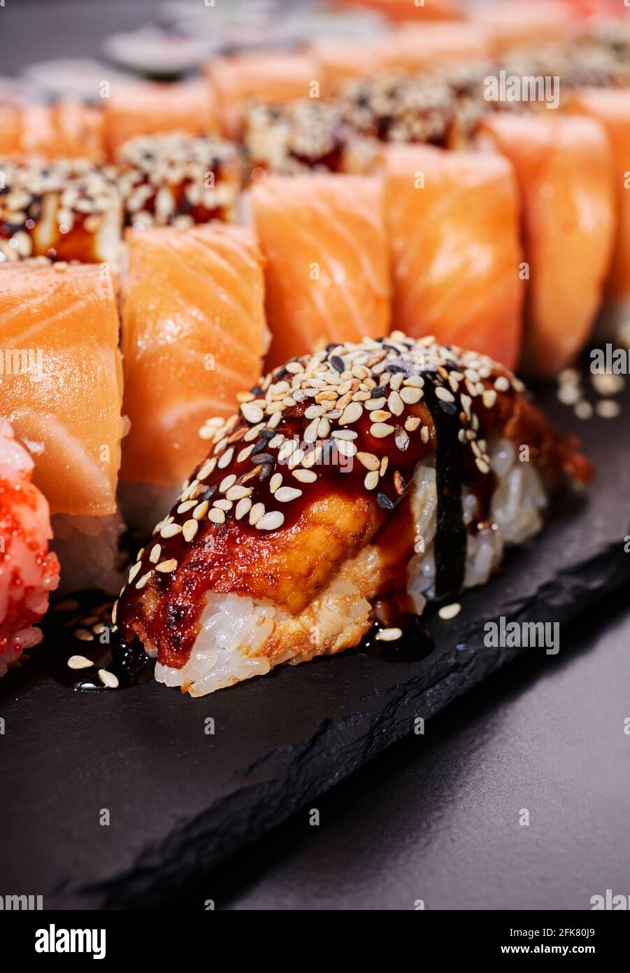 Un pezzo di sushi nigiri si trova su una tavola di pietra nera su uno sfondo di Rolls Philadelphia. Concetto di deliziosa cucina tradizionale giapponese, delici Foto Stock
