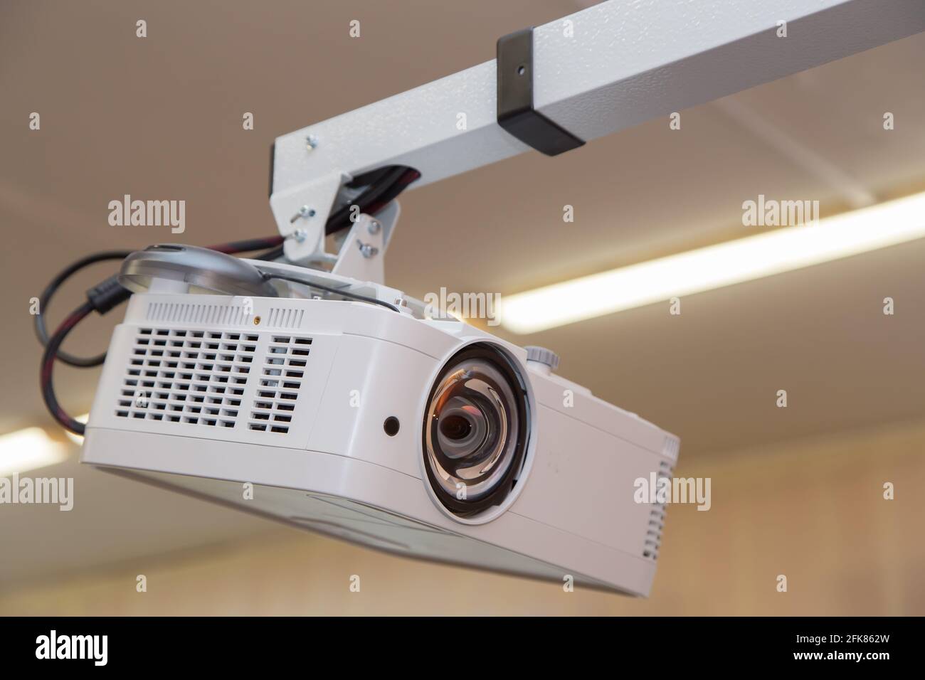 Un videoproiettore bianco è appeso al soffitto con un braccio lungo. Le  lampade fluorescenti sono accese sul retro. Obiettivo rotondo con una musa  astratta Foto stock - Alamy