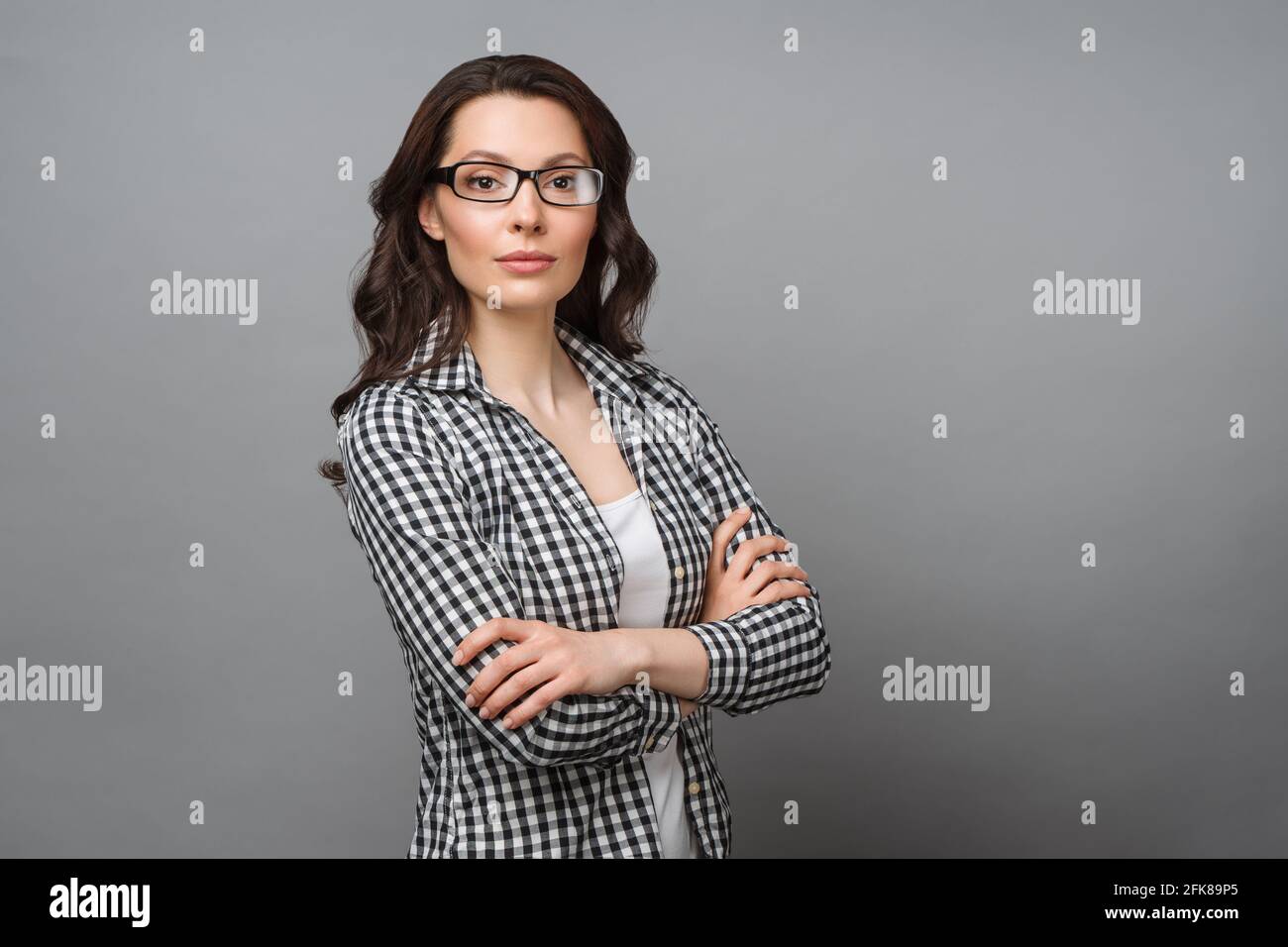 Ritratto aziendale di una giovane donna. Una bruna affascinante con occhiali guarda la macchina fotografica, incrociando le braccia sul petto. Foto Stock