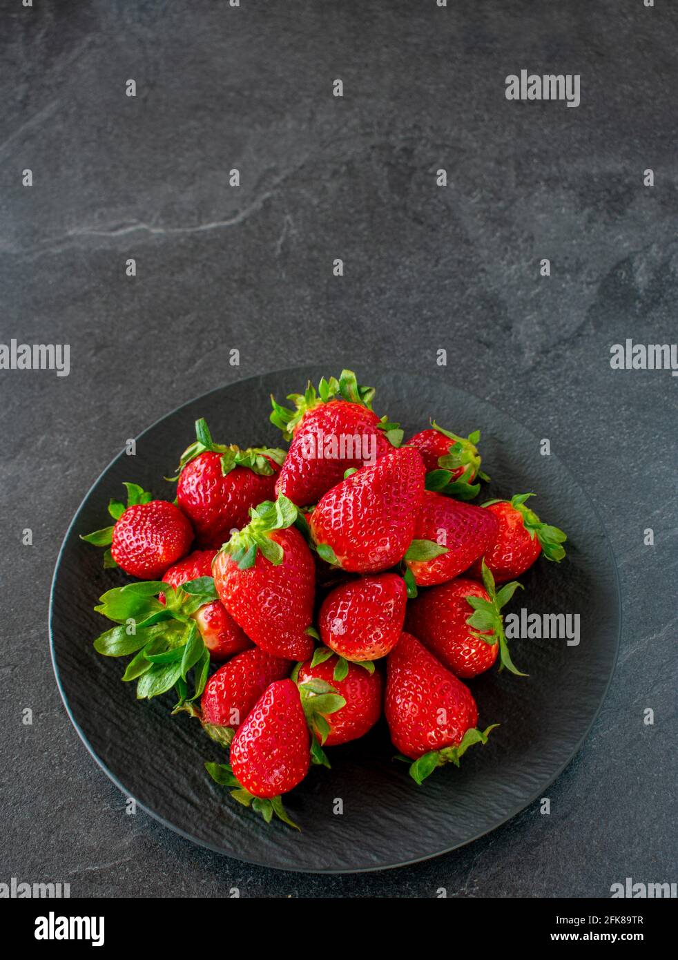 Fragole fresche e mature con gambo e foglie su un piastra scura su sfondo scuro del tavolo con spazio per la copia Foto Stock