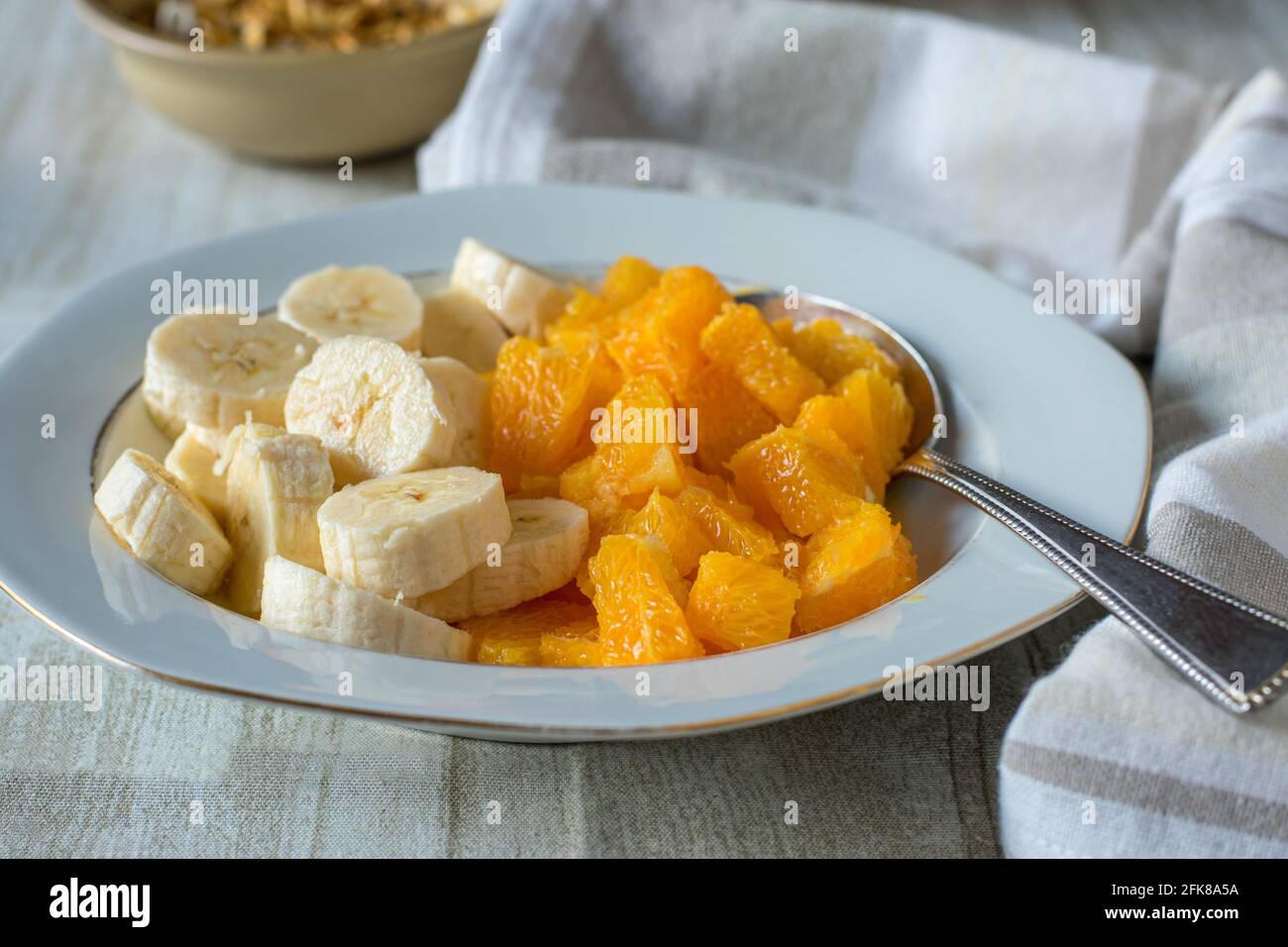 Un piatto con banane tritate e arance servite su un tavolo di legno bianco a casa. Vista in primo piano Foto Stock