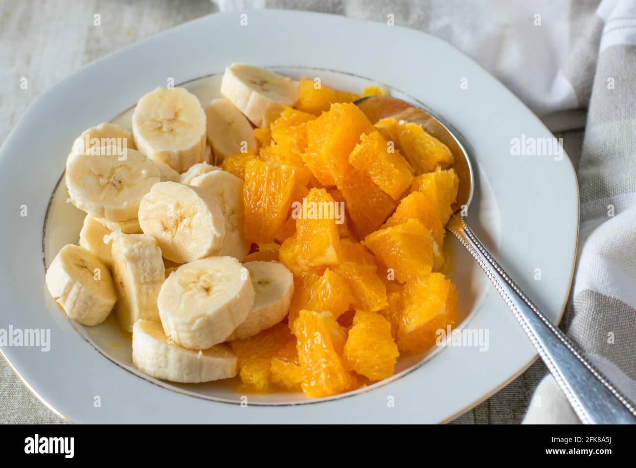 Un piatto con banane tritate e arance servite su un tavolo di legno bianco a casa. Vista in primo piano Foto Stock