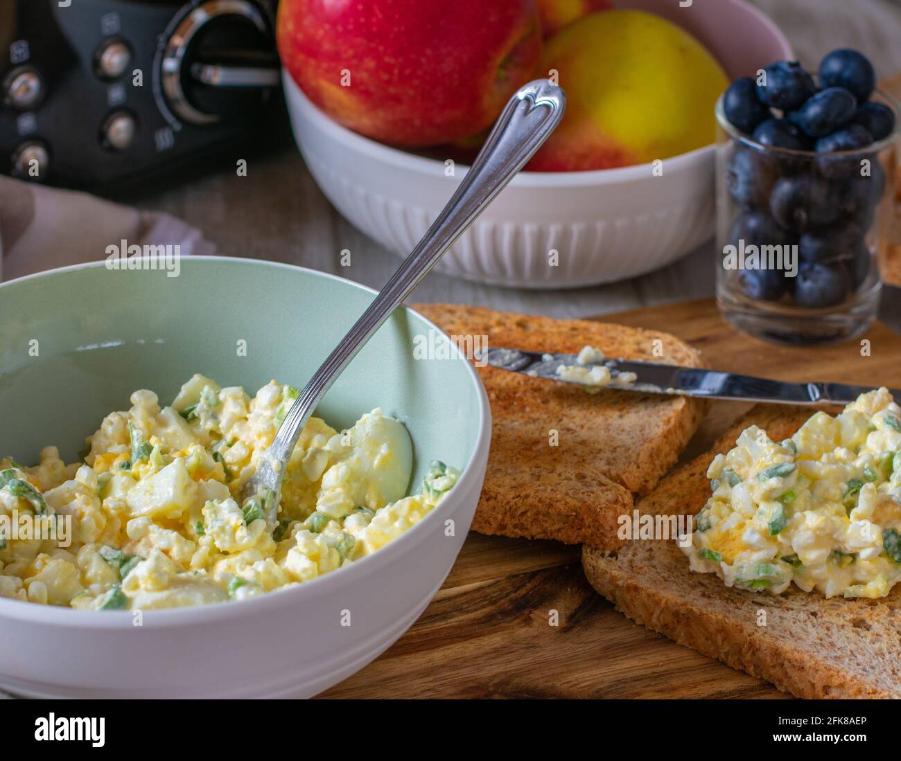 Colazione ad alta concentrazione di proteine con insalata di uova a basso contenuto di grassi preparata con formaggio di cottage, uova bollite e erba cipollina serviti in ciotola con pane tostato integrale su un tavolo Foto Stock