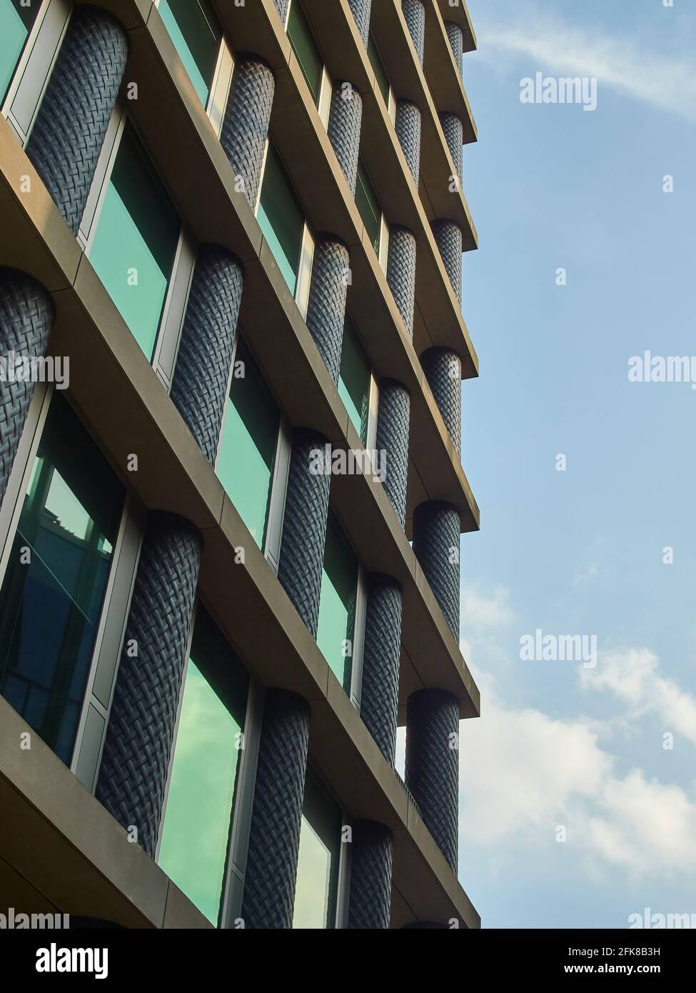 Un dettaglio di un edificio di uffici di nuova costruzione, parte di un progetto di rinnovamento urbano più generale, contro un cielo di primavera blu luminoso e punteggiato da nuvole. Foto Stock