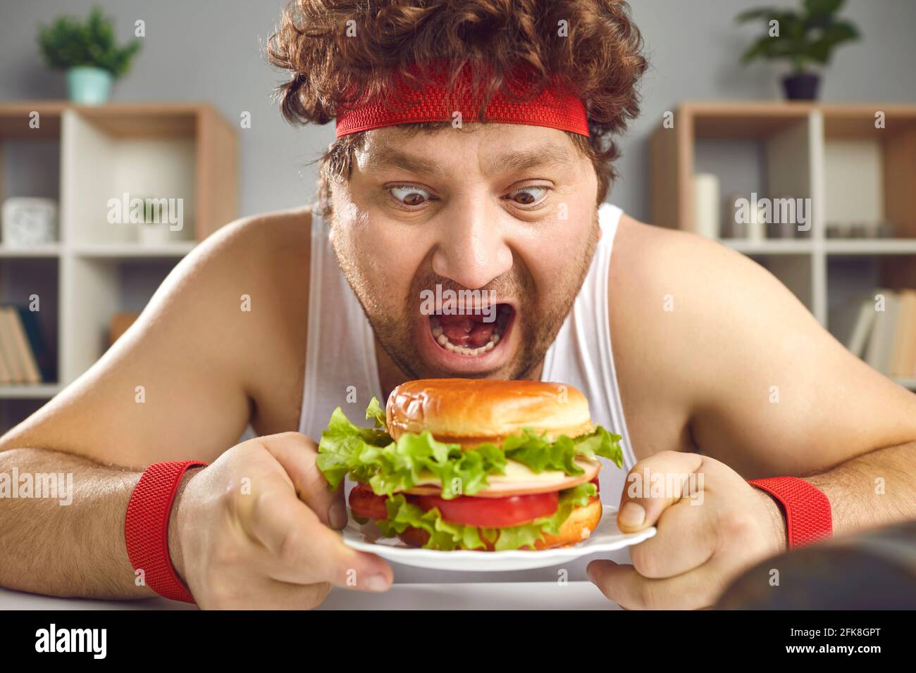 Affamato uomo chubby pazzo in abbigliamento sportivo mangiare hamburger fast food verticale Foto Stock