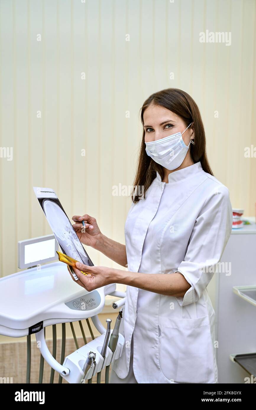 un ortodontista sul suo posto di lavoro che indossa una maschera tiene un immagine dei denti Foto Stock