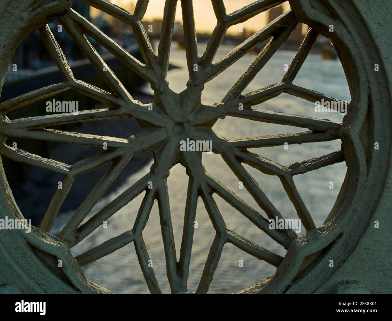 Un tramonto dorato sfocato su uno skyline della città, visto attraverso un pezzo di ferro ornato nelle ringhiere di un ponte sul Tamigi. Foto Stock