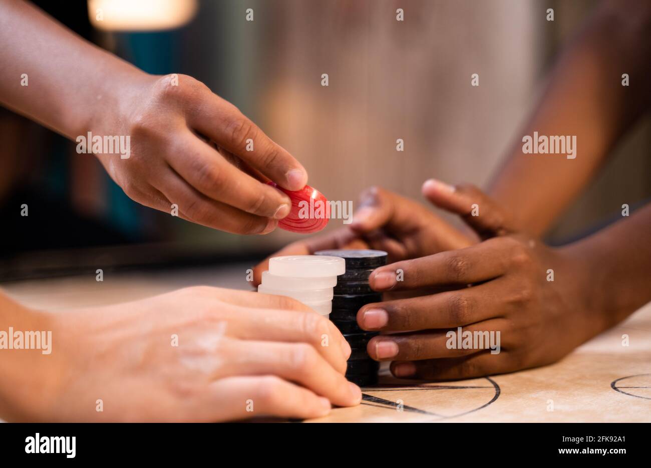 Primo piano diverse mani multietniche bambini organizzare carom gioco da tavolo monete prima di giocare - concetto di lavoro di squadra, la cooperazione e il successo. Foto Stock