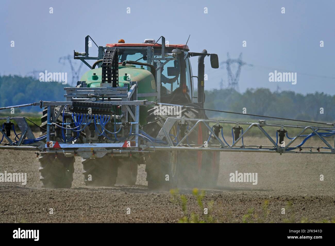 Trattore che spruzza campo di grano con spruzzatore, erbicidi e pesticidi. Spray con pesticida primaverile. Trattamento chimico agricolo. Foto Stock