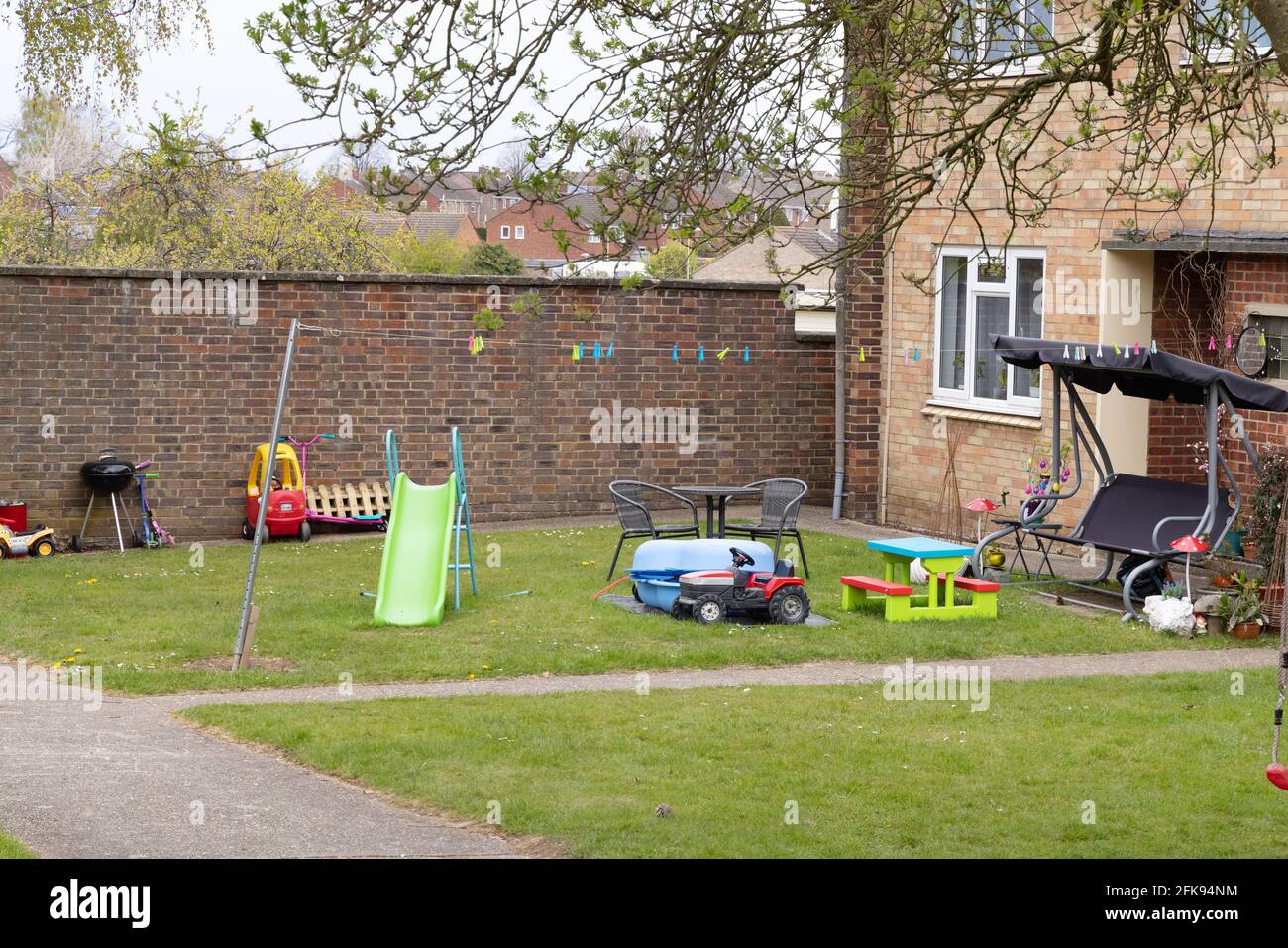 Giardino anteriore UK; un giardino anteriore di una casa a schiera piena di giocattoli per bambini; Suffolk UK, esempio di stile di vita britannico e casa di famiglia UK Foto Stock
