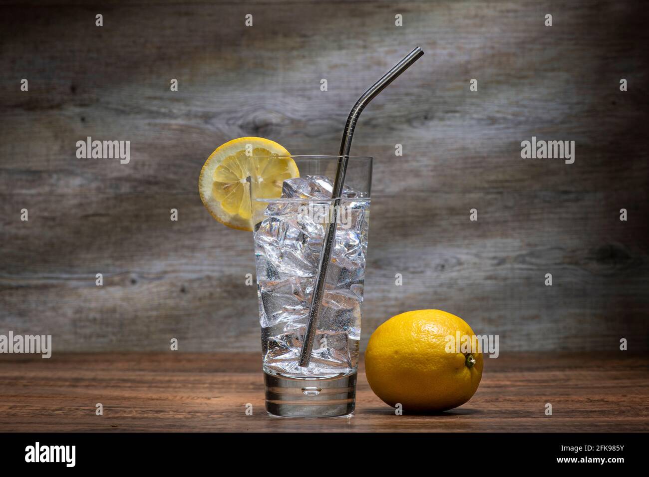 Bicchiere d'acqua con ghiaccio e limone e cannuccia in acciaio inox in un bicchiere di highball. Foto Stock