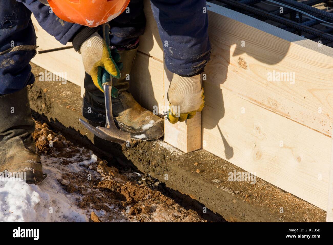 Un lavoratore martella un chiodo in un cantiere. Installazione di casseri in legno. Lavori di costruzione Foto Stock