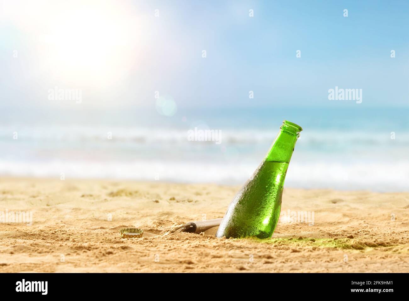Dettaglio di una bottiglia di birra fresca seppellita per metà nella sabbia su una spiaggia in una giornata calda. Dettaglio della vista frontale. Foto Stock