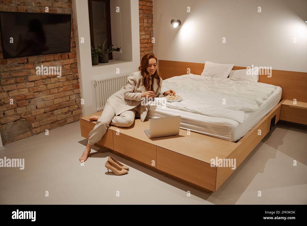 Una giovane donna d'affari o un tirocinante in viaggio d'affari dopo una dura giornata guardando film o serie TV su un computer portatile in una camera d'albergo. Modello femminile con capelli rossi Foto Stock