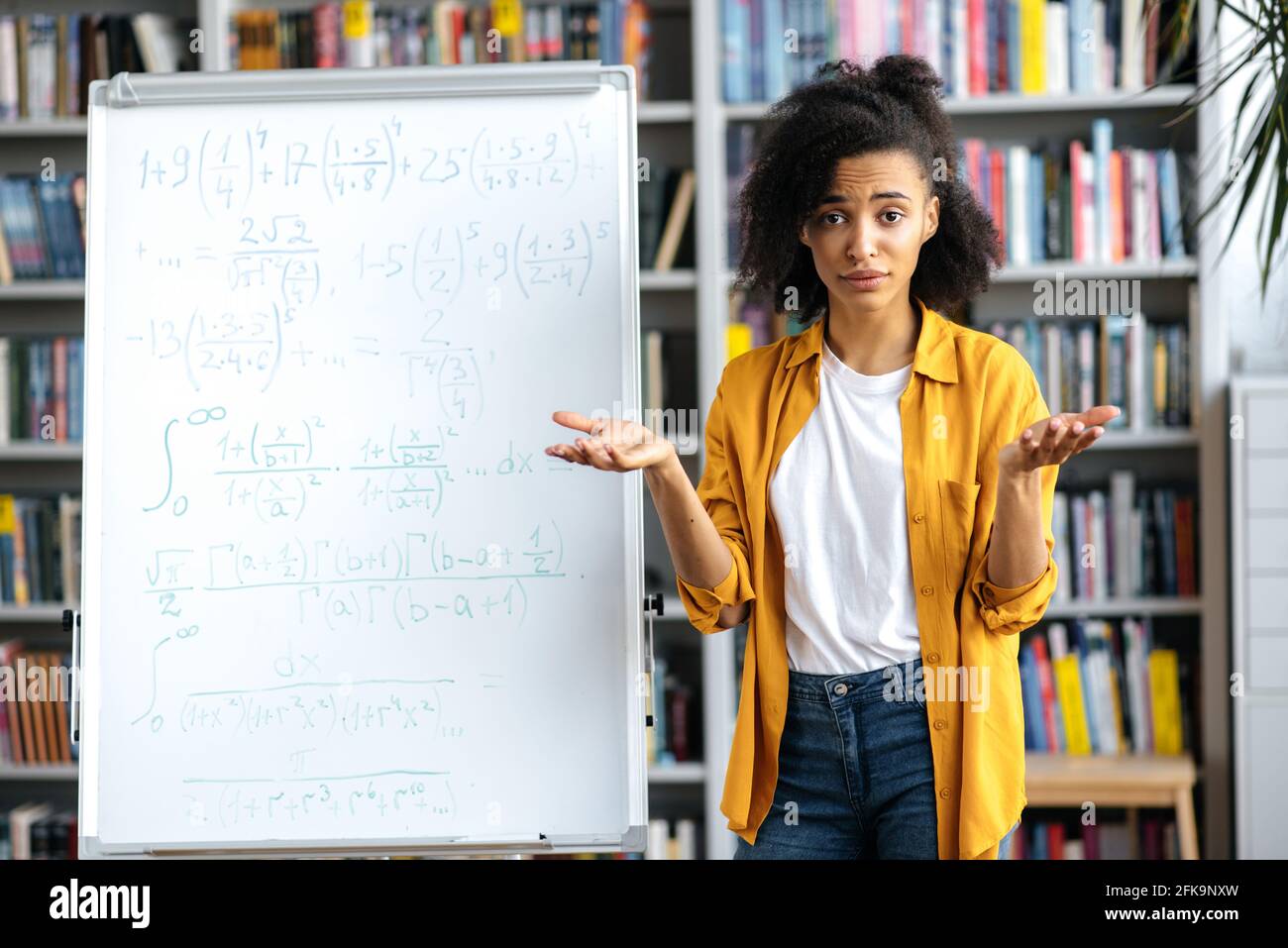 Ritratto di giovane donna afro-americana confusa in piedi vicino a lavagna bianca, in abiti casual, conduce lezioni, comunicazione online con gli studenti, guardando la macchina fotografica a sorpresa Foto Stock