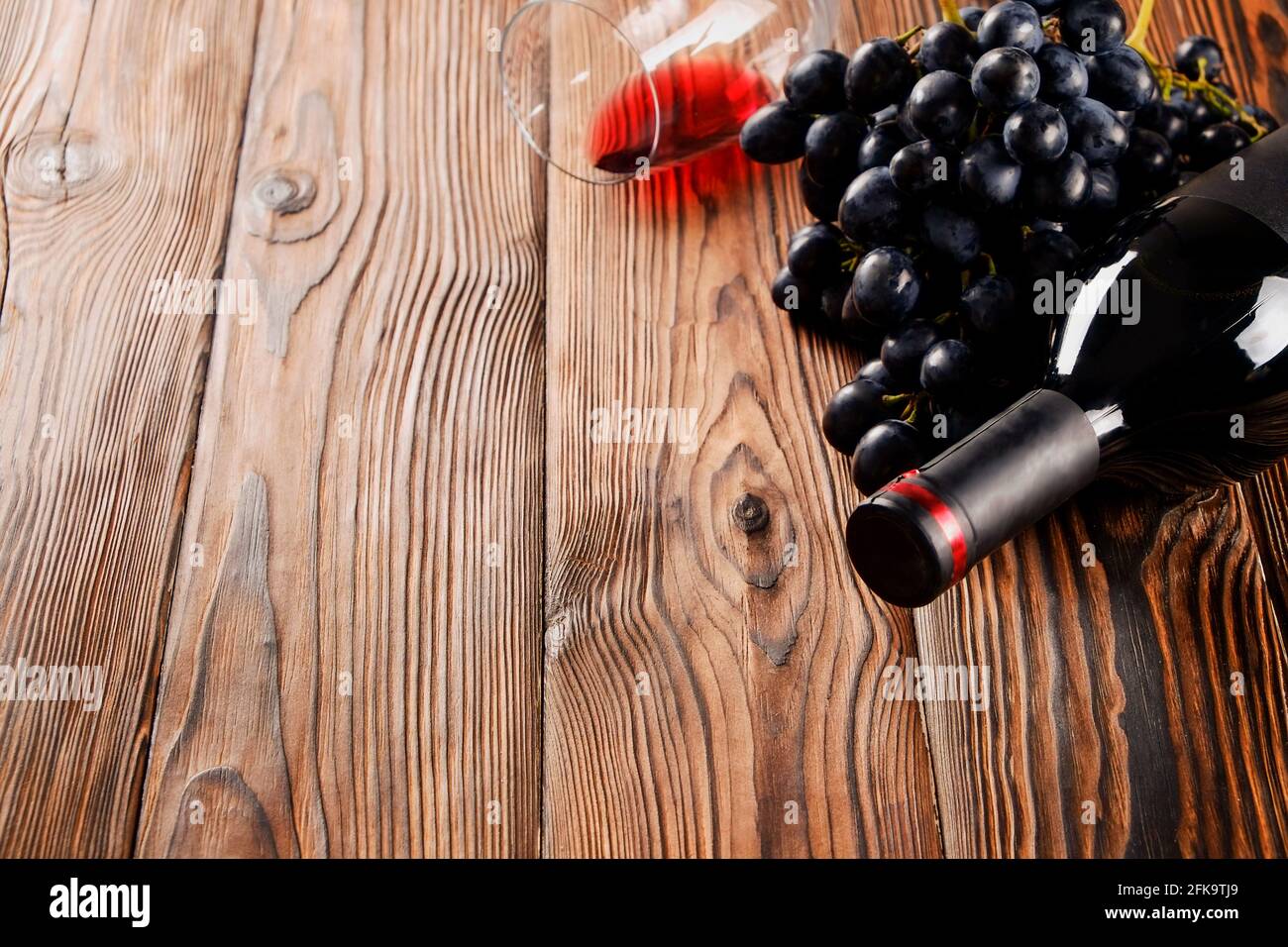 Bottiglia di vino rosso vintage con etichetta nera opaca, cavatappi e grappoli di uva su sfondo di tavola in legno. Bottiglia costosa di cabernet sauvignon Foto Stock
