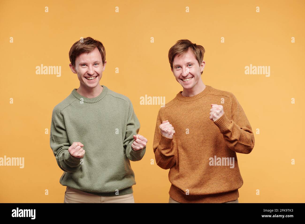Ritratto di fratelli gemelli emozionali eccitati in casual pullover fare sì gesti su sfondo arancione Foto Stock