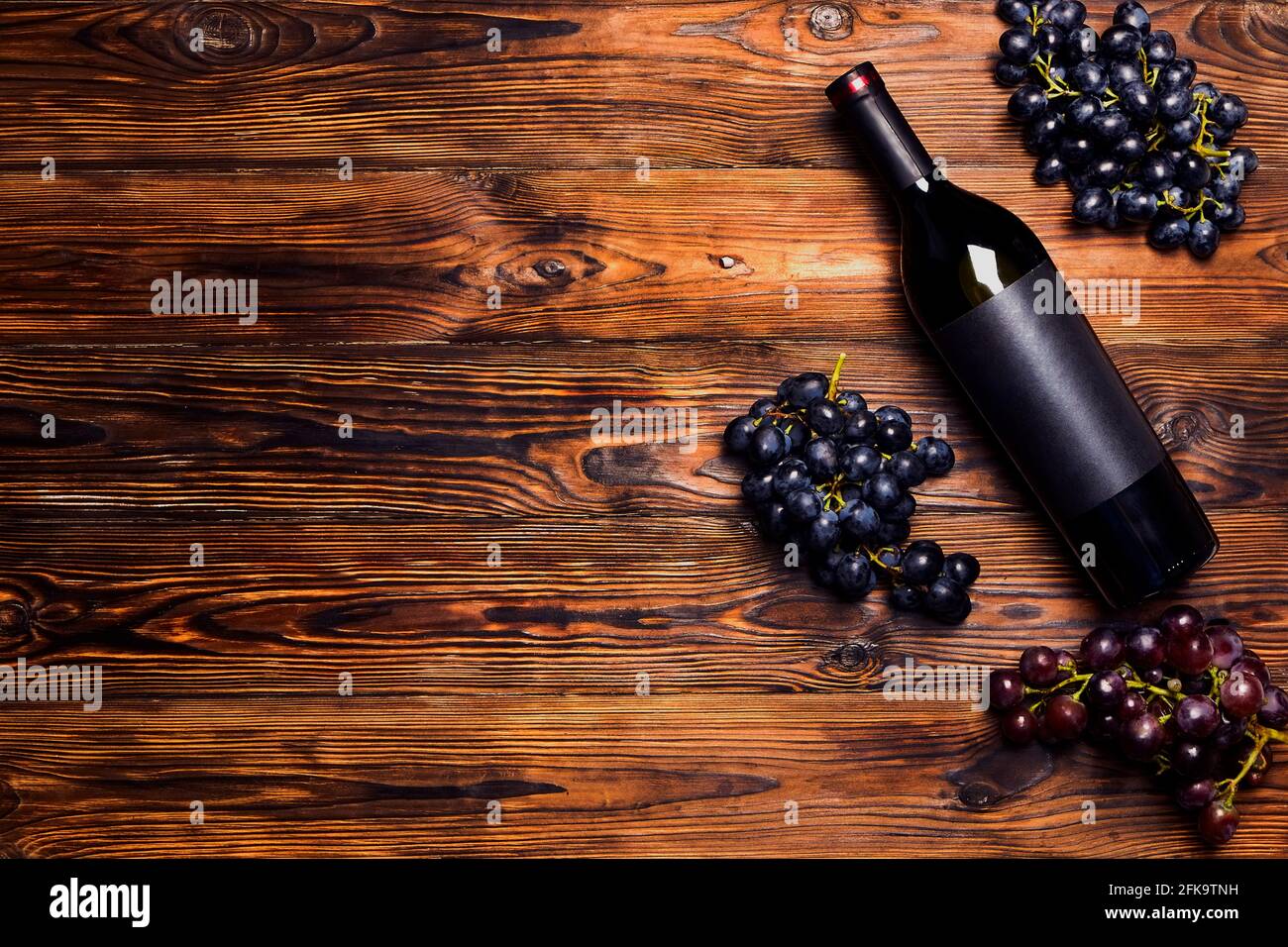 Bottiglia d'annata non aperta di vino rosso con etichetta nera opaca bianca e grappoli di uve mature su sfondo di tavola in legno. Costosa bottiglia di cabernet sau Foto Stock