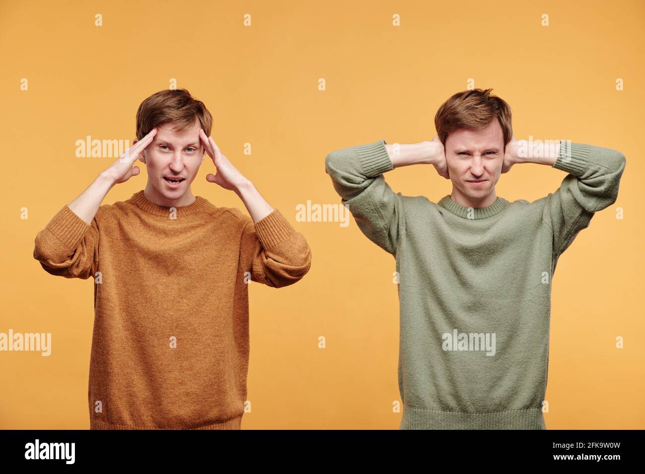 Ritratto di gemelli infastiditi in pullover su sfondo arancione: Uno di loro coprendo le orecchie con le mani altre tenendo le mani vicino fronte Foto Stock