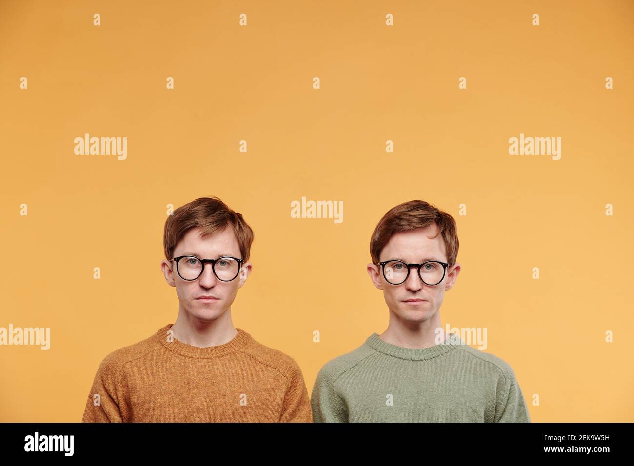 Ritratto di bei gemelli giovani in occhiali e maglioni in piedi su sfondo arancione Foto Stock