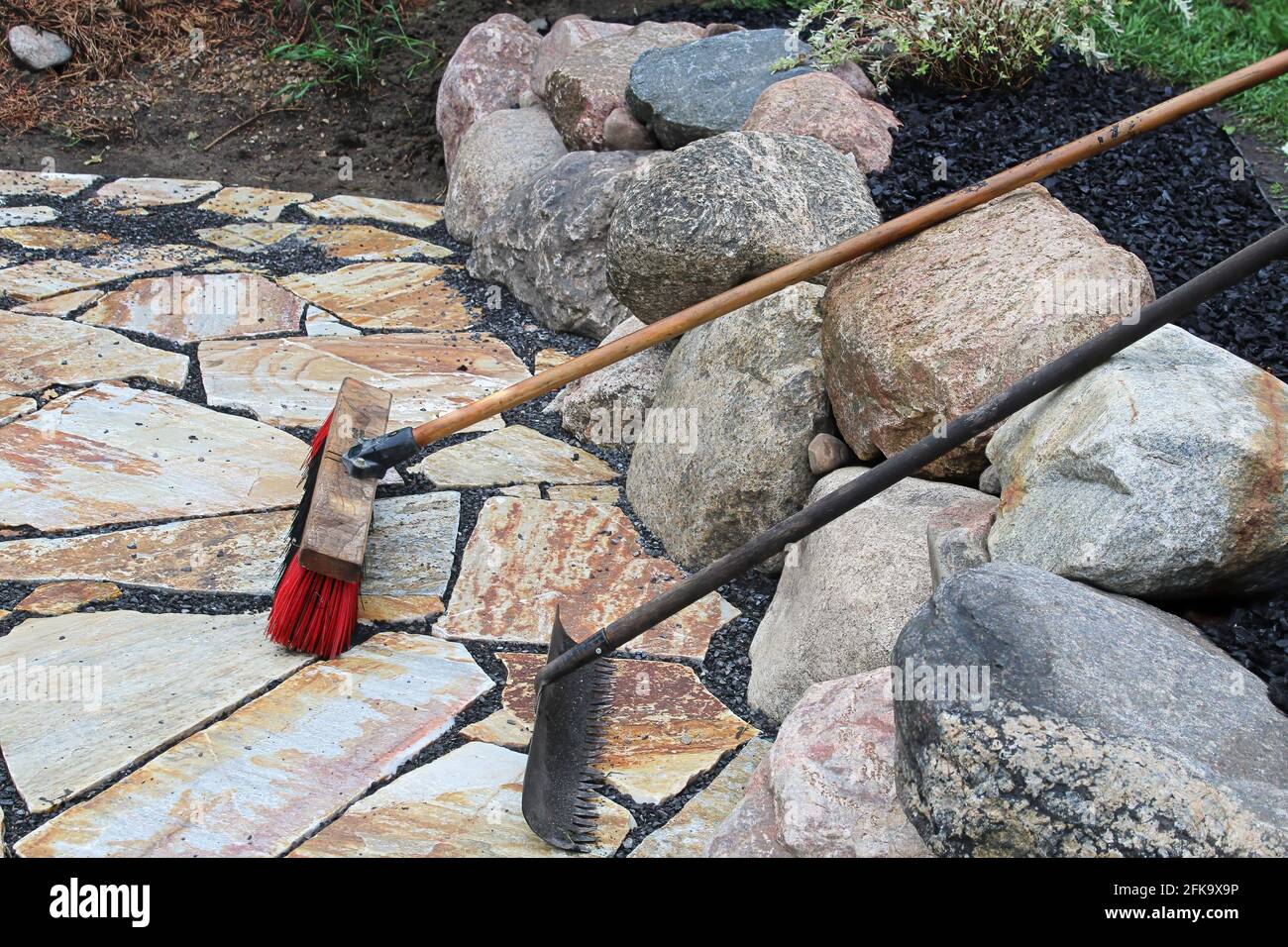 Un rastrello e una scopa utilizzati sulle pietre del patio Foto Stock