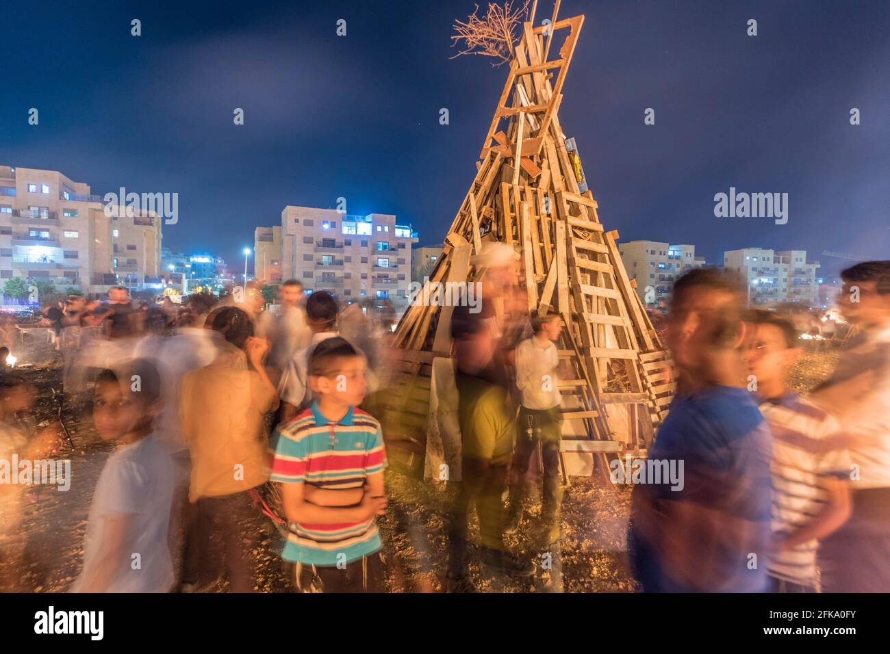 I bambini si trovano nei pressi di una pira spenta, pronta per la festa ebraica di Lag Baa'Omer, che si svolge ogni 18 del mese ebraico Iyar. È consuetudine durante questa vacanza fare incendi. Quest'anno, a causa del pericolo di incendio, tutti gli incendi sono stati concentrati in pochi siti, da cui il gran numero di piri. Foto Stock