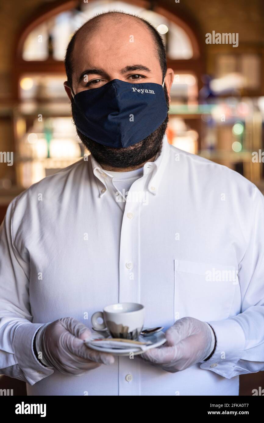 Ritratto di un cameriere che indossa una maschera e guanti per motivi di sicurezza COVID all'interno di un ristorante Foto Stock