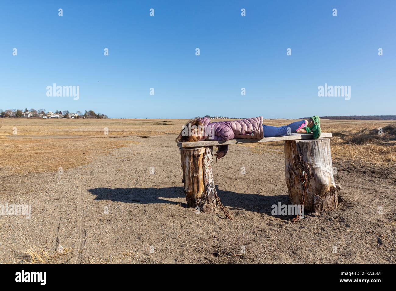 Bambina che si posa su un banco di legno che si affaccia su una palude Foto Stock