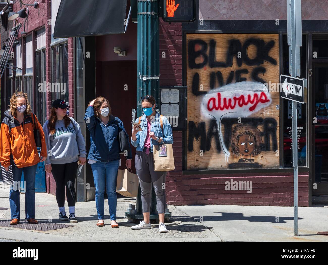 ASHEVILLE, NC, USA-25 APRILE 2021: Quattro giovani donne bianche con maschere COVID, in piedi sulla strada accanto alla finestra con il segno 'Black Lives Always Matter'. Foto Stock