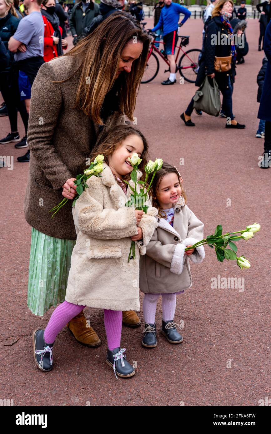 Una famiglia paga i loro rispetti al principe Filippo che recentemente è passato via dalla posa dei fiori ai cancelli di Buckingham Palace, Londra, Regno Unito. Foto Stock