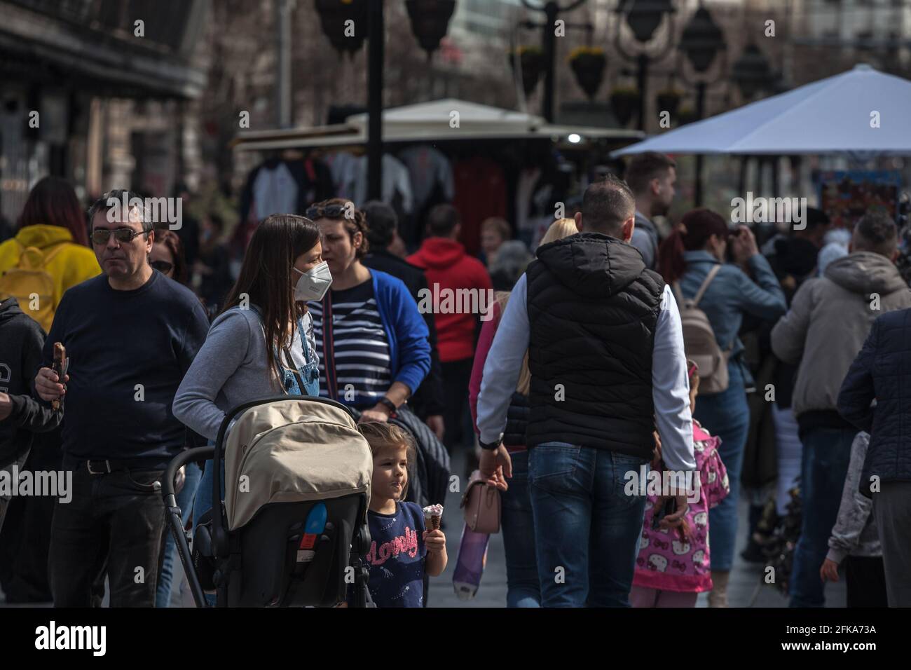 Immagine di una famiglia fatta di una donna e di un passeggino con il suo ragazzo che cammina nel mezzo di una folla con una maschera facciale, a Belgrado, Serbia, durante Covid 1 Foto Stock