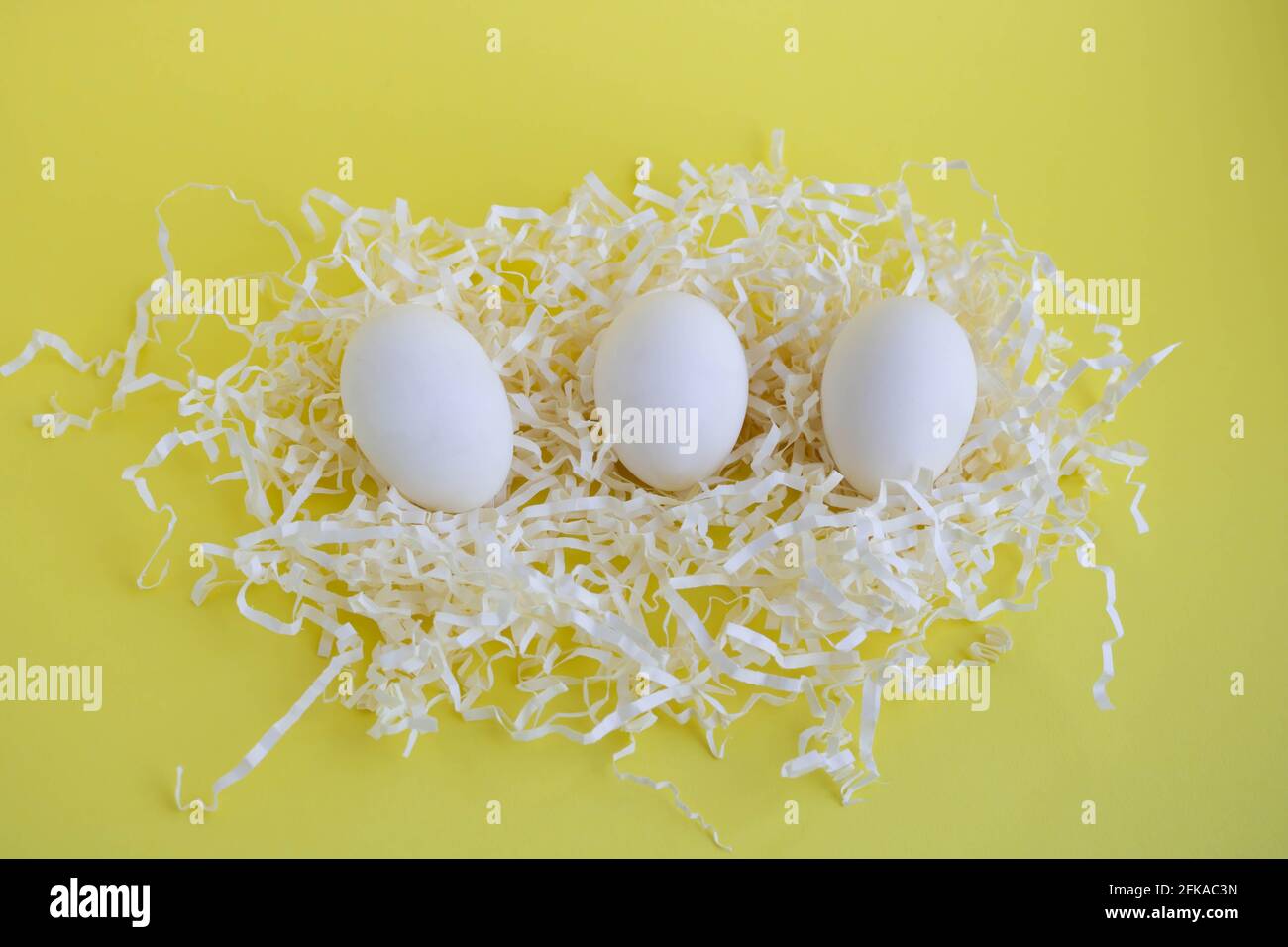 Tre uova bianche in Tinsel su sfondo giallo. Concetto di Pasqua. Foto Stock
