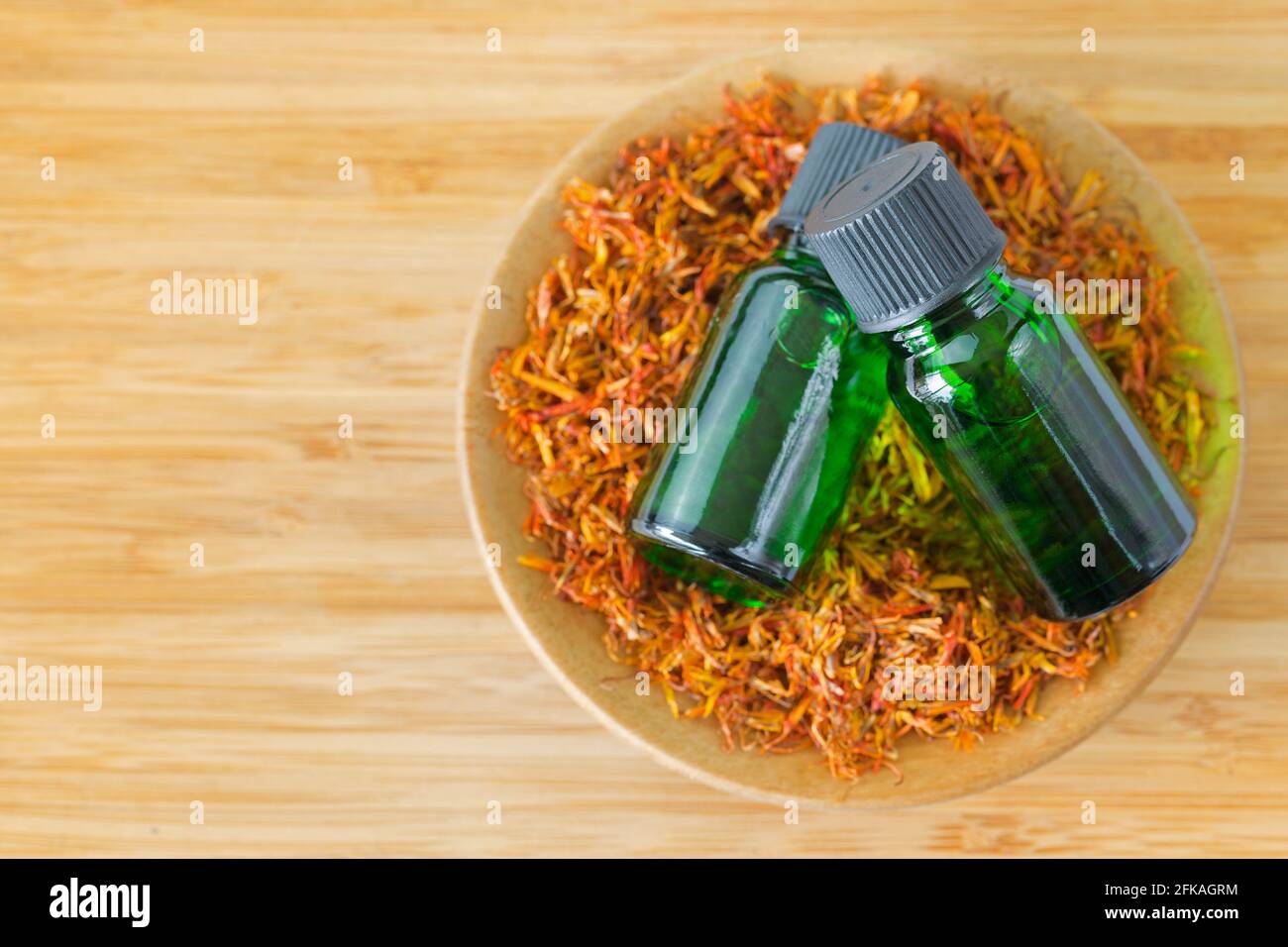 Estratto di olio concentrato puro di Safflower Essential in flacone verde ciotola di pianta di cartamo essiccata su fondo di legno con copyspace (Cartamus tinto Foto Stock
