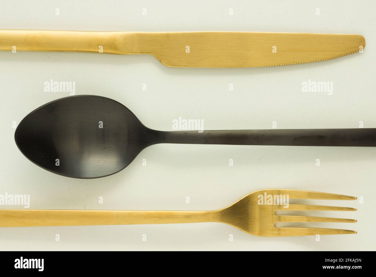 Forchetta dorata e nera, coltello e cucchiaio su sfondo bianco; posate; taglio; posa creativa piatta; Art Deco Foto Stock