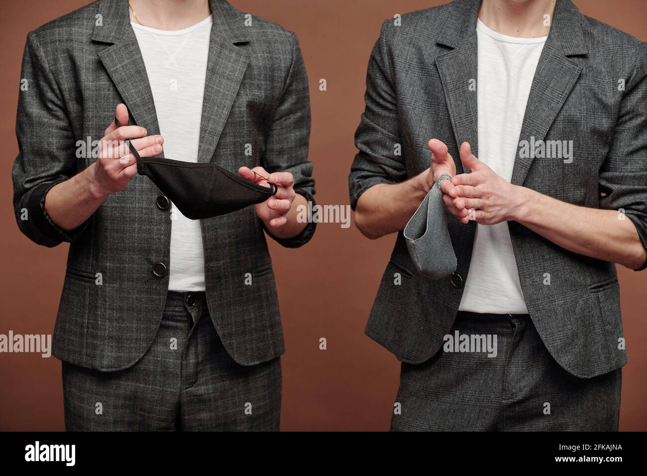 Primo piano di uomini irriconoscibili in abiti casual eleganti che tengono un panno maschere su sfondo marrone Foto Stock