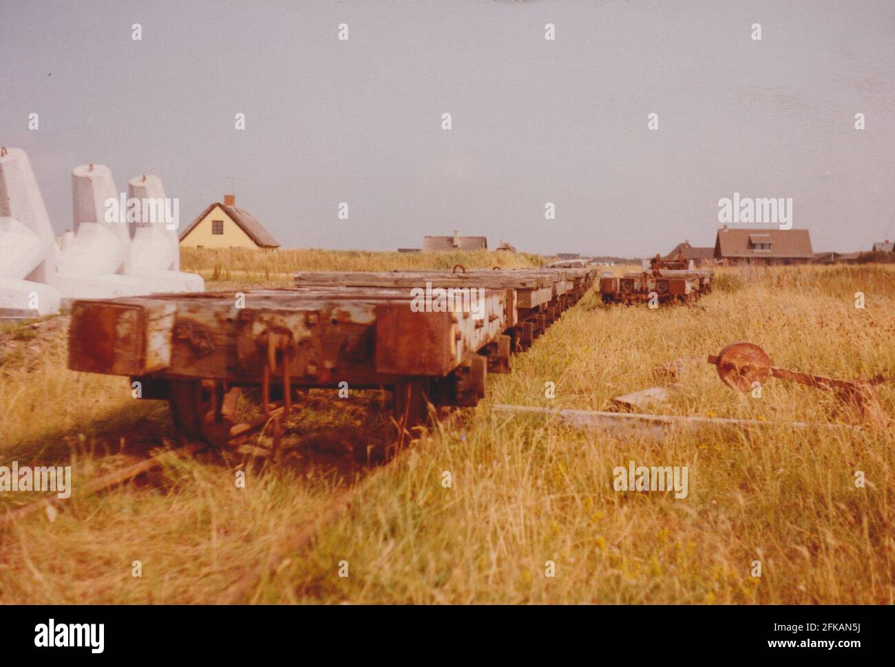 Agger, Danimarca - 1983: Le officine della manutenzione della conca 'Vandbygningsvsenet' con i binari ferroviari a scartamento ridotto (785mm) ora rimossi. Carrelli di rotaia disposti per la rottamazione. Foto Stock